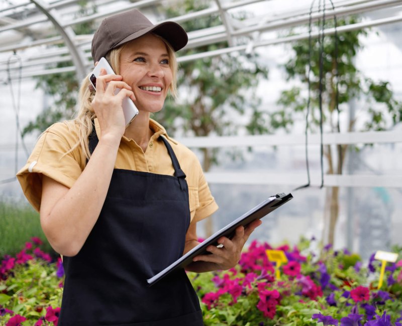 Pretty female florist with clipboard talking on the phone in a flower greenhouse